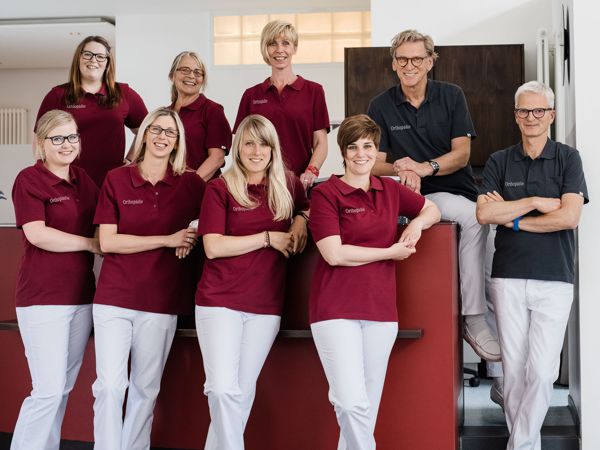 Praxispersonal von neun Personen mit passender Arbeitskleidung.